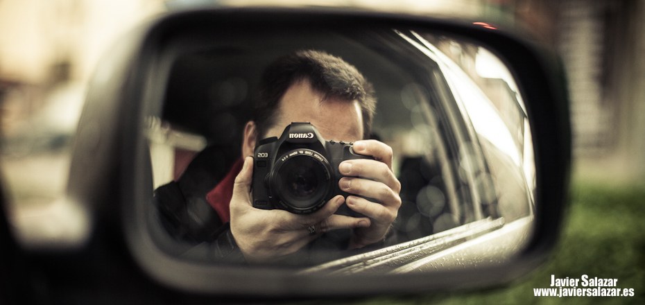 Autorretrato de Javier Salazar con una cámara, reflejado en el espejo retrovisor de un coche